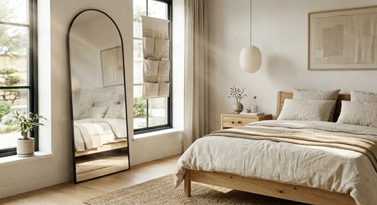 Minimalist neutral bedroom featuring a wooden bed, linen bedding, large arched mirror and hanging fabric organiser.